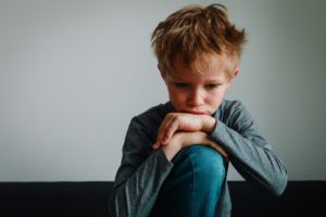 Sad young boy sitting alone representing emotional trauma after alleged abuse in residential treatment